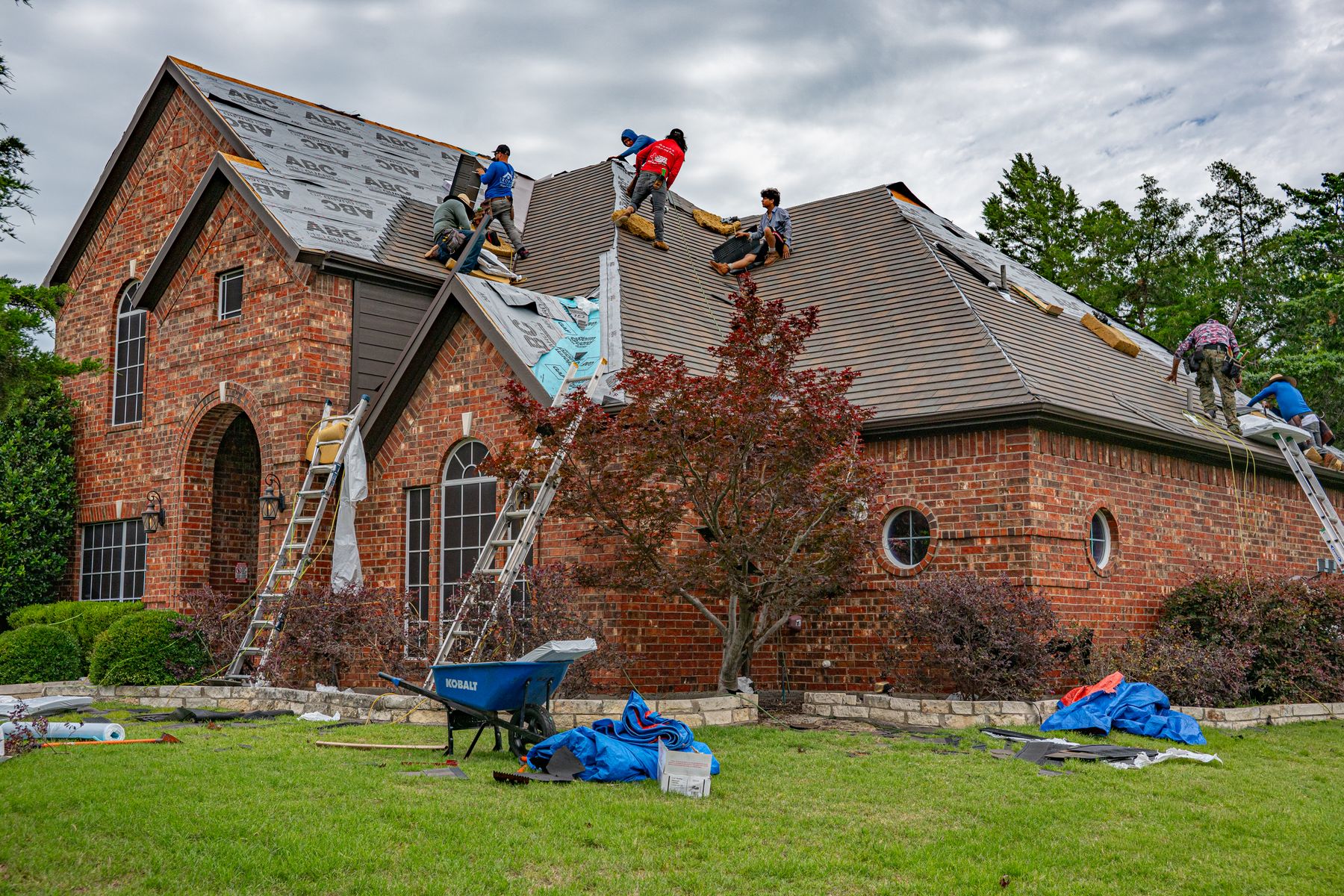 A Ridgeline crew on the roof of a brick house, mid tear-off
