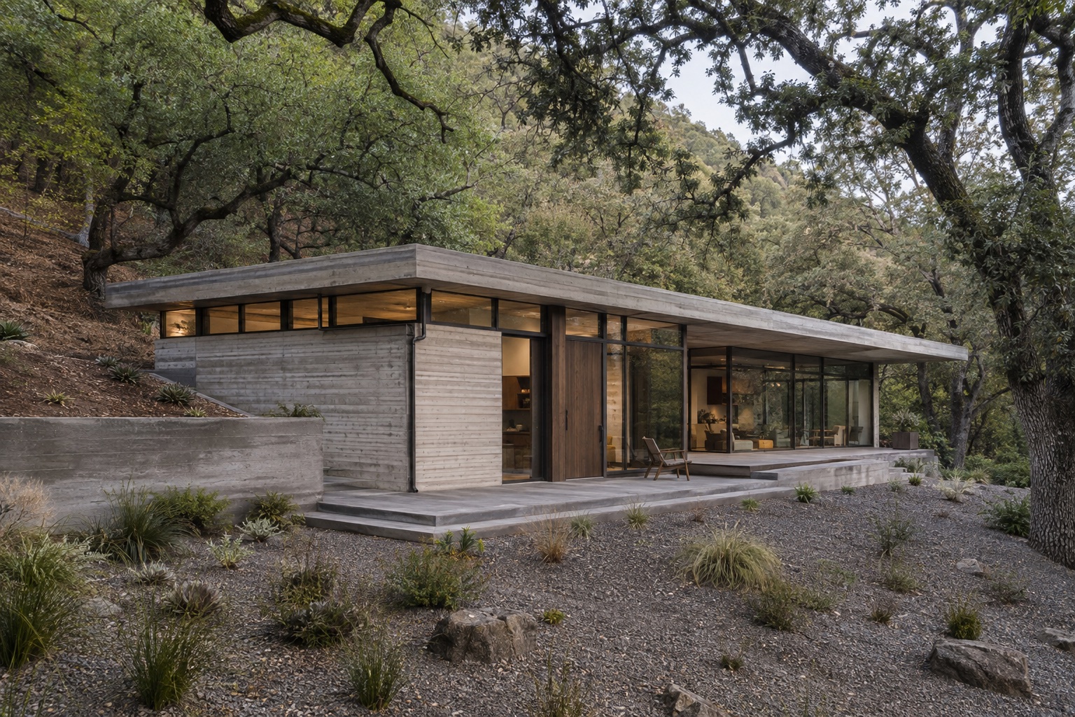 A concrete and timber house nestled into an oak-covered hillside, with a lived-in terrace and broad glazing.